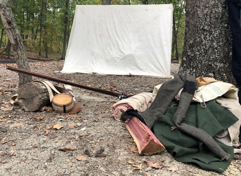 A old fashioned white canvas tent is shown with various camping supplies scattered about.