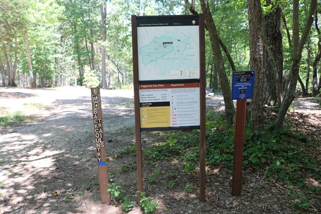 A large billboard with a trail map is along a trail in the woods