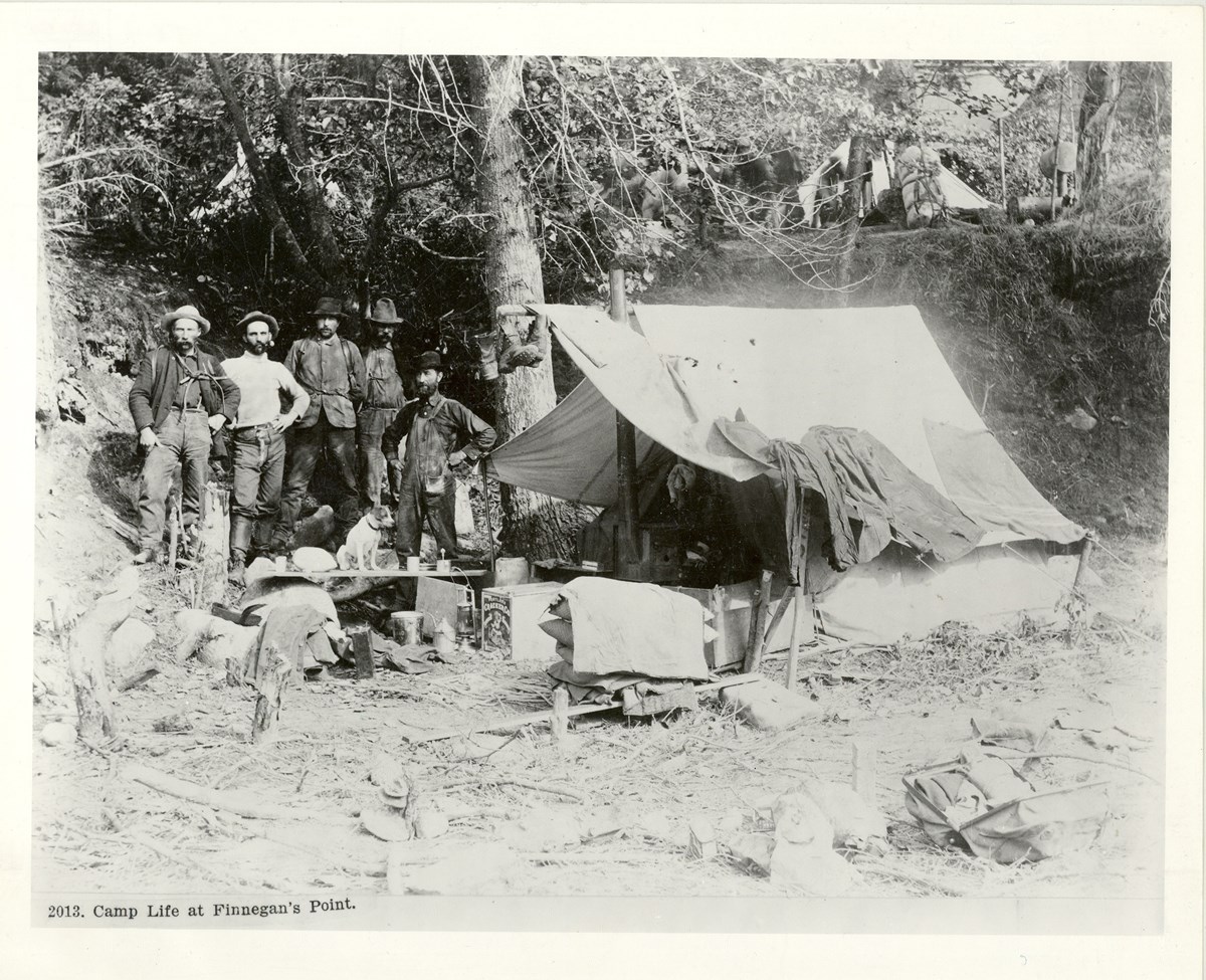 Five men stand with a canvas tent and supplies.
