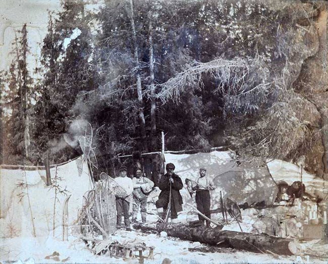 People stand in the snow among trees and canvas tents