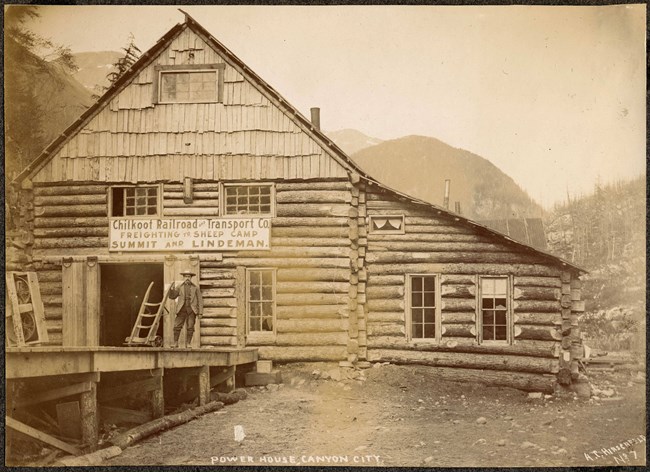 Black and white photo of a large log cabin with a sign reading "Chilkoot Railroad and Transport Co"