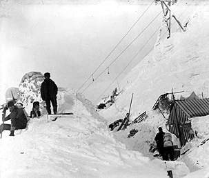 Black and white photo of men standing on deep snowpiles