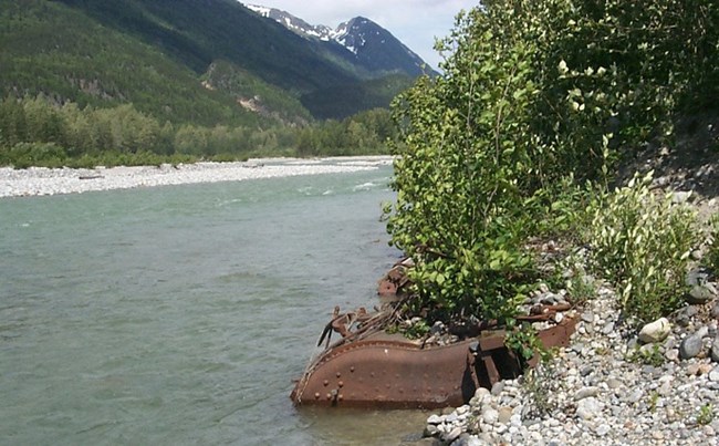 Large rusted metal embedded at edge of river