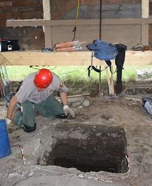 Ranger in hard hat kneels next to a square hole by an upraised building