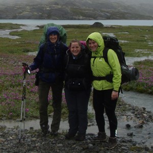 Three hikers stand in the rain near a stream