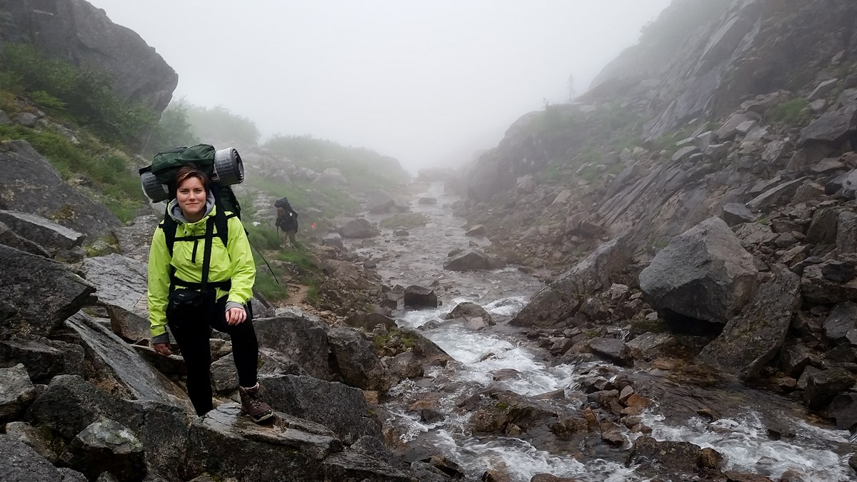 A backpacker poses along a rocky creek in the fog