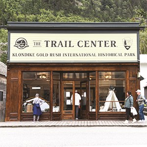 People walking by a wooden building titled "The Trail Center"