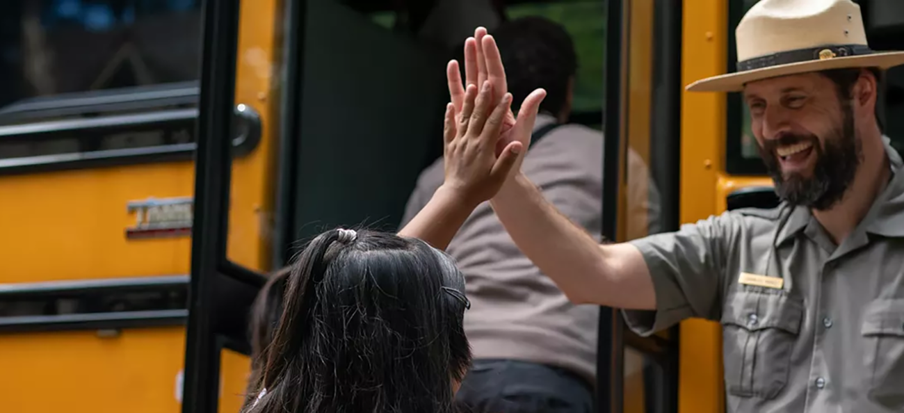 A person wearing a ranger hat high fives and 4th grader.