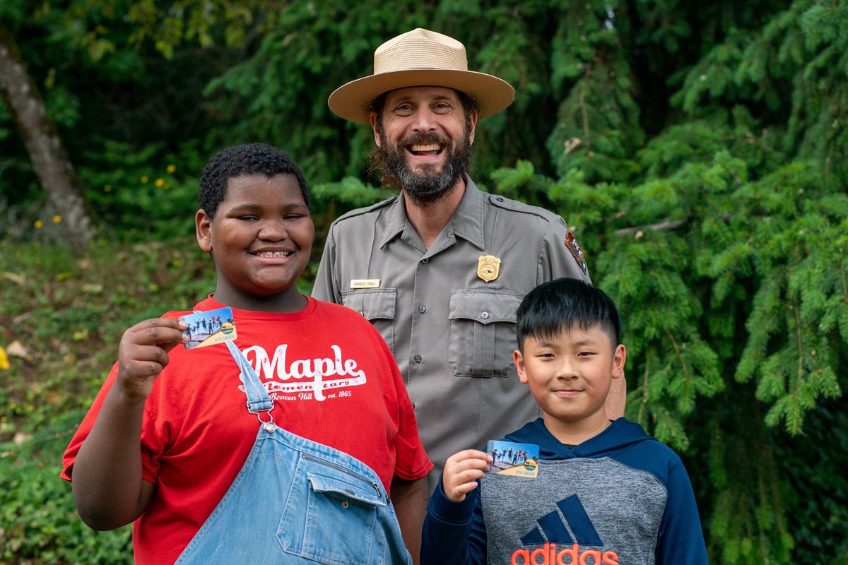 a ranger poses with two children holding up park passes