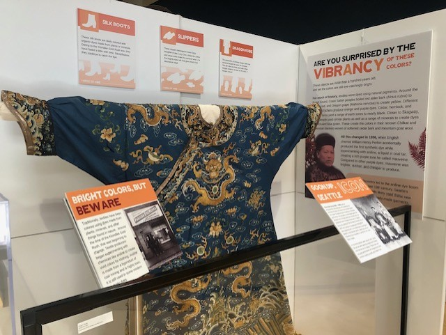 Blue and gold robe, called a Dragon Robe, on display with informational signs surrounding it.