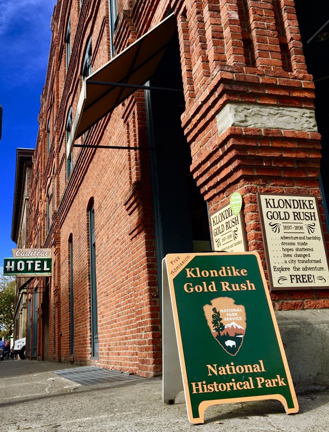 A sidewalk view of a sandwich board that says Klondike Gold Rush National Historical Park