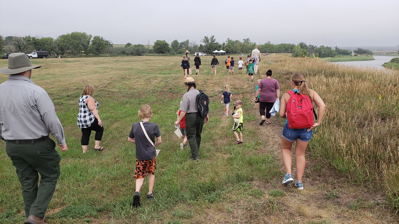 Kids, teachers, and rangers walk toward archeology site.