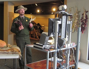 Male ranger holds dried red corn in the museum in front of a video camera and tv screen
