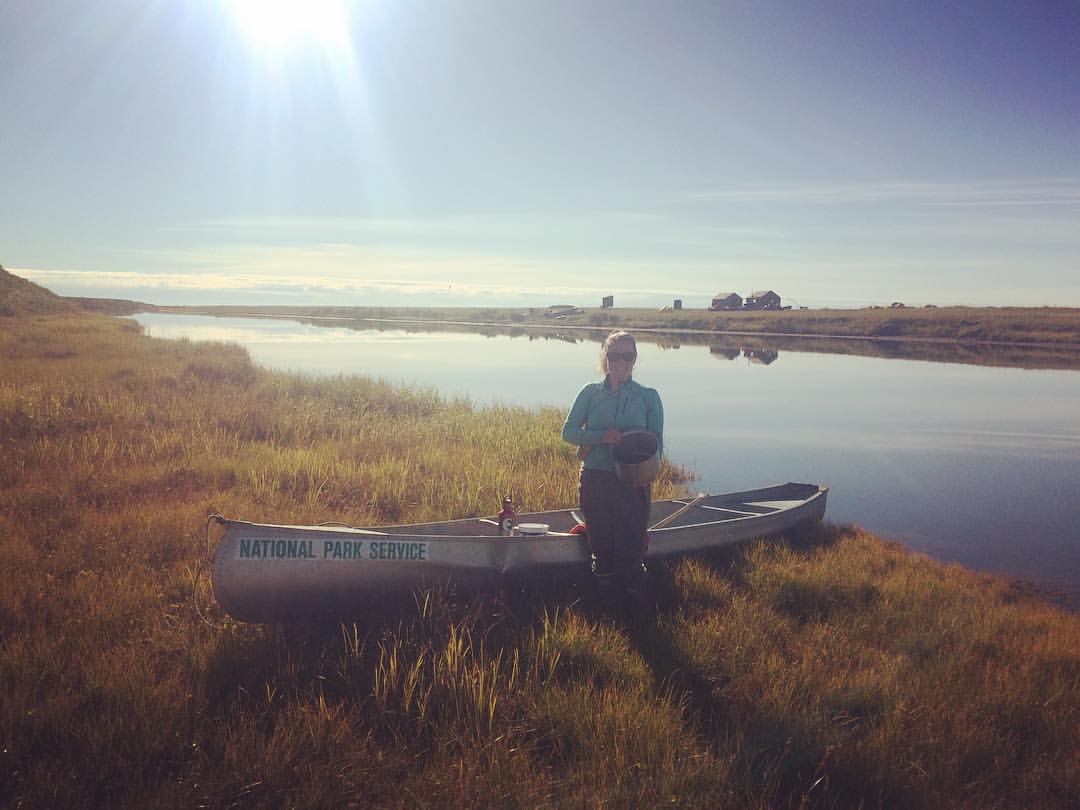 Hannah Atkinson Anigaaq Ranger Cabins Hannah stands next to a canoe and small pond holding a bucket of berries