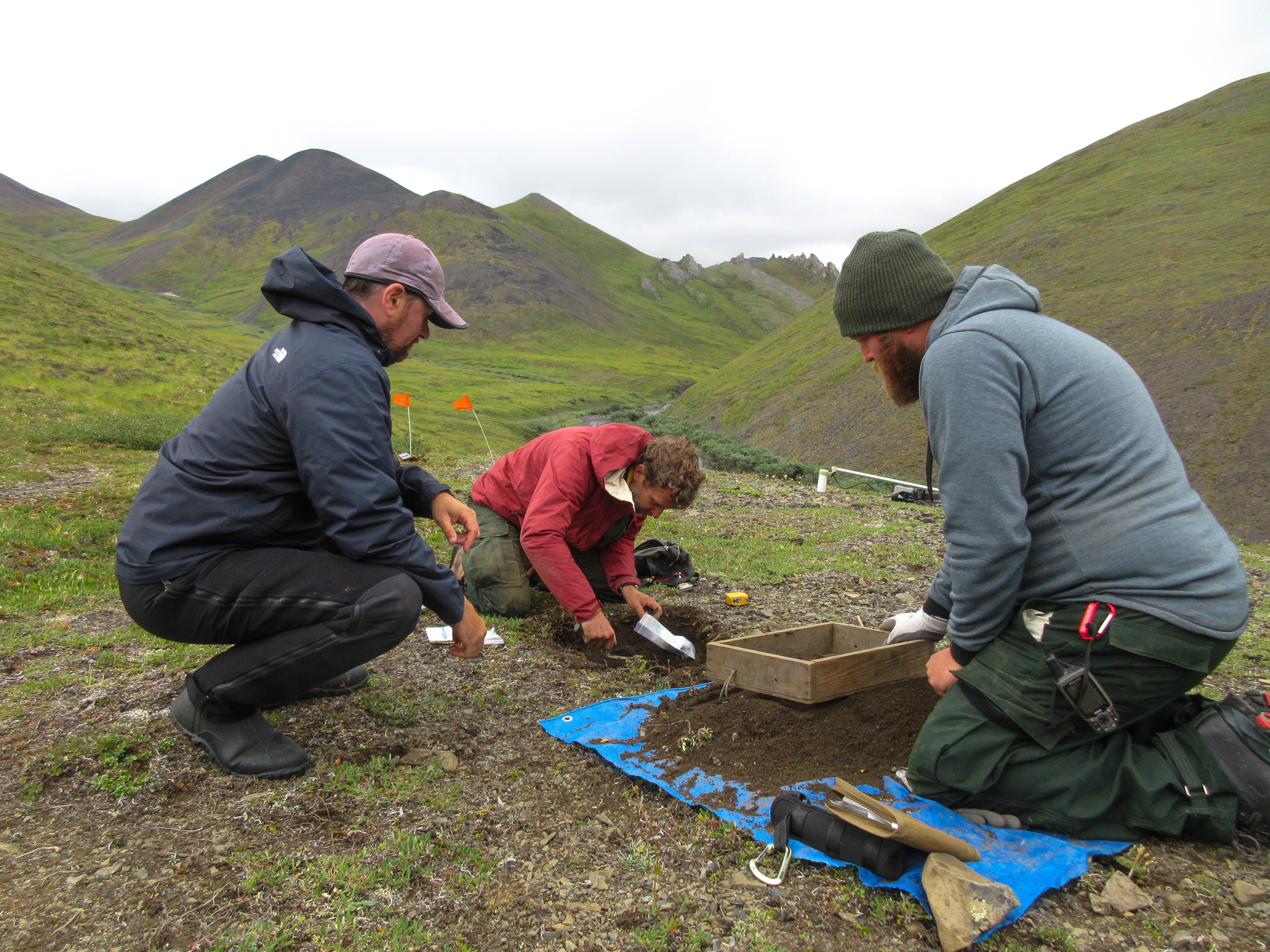 Justin doing archaeology work in the field with colleagues. Three men use shovels to dig up soil to take samples of the soil