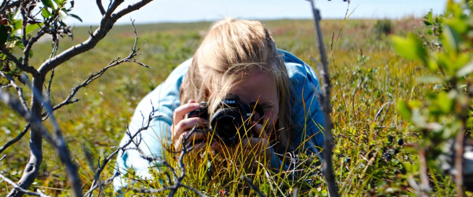 Girl lying on grassy tundra with camera