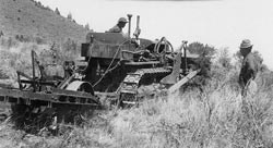 A historic photo of a machine and two men clearing brush
