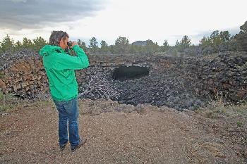 A visitor scans the lava tube collapse along the Heppe Cave Trail (cave entrance seen in the distance).