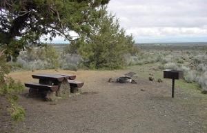 Campsite with table, fire pit, cooking grill, and juniper