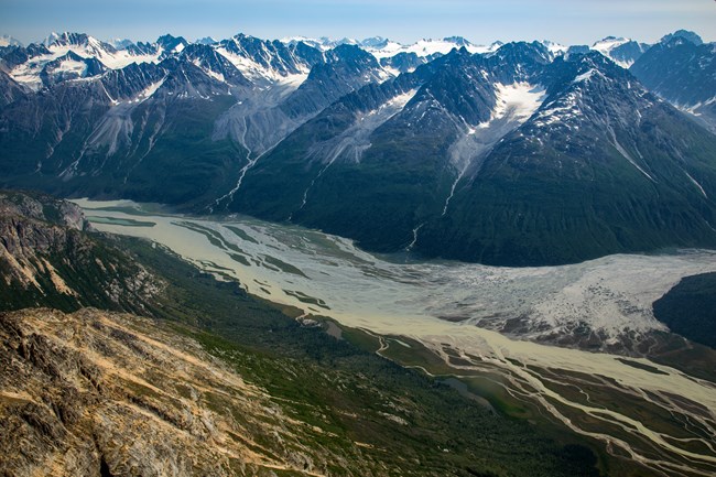 a braided river cuts through jagged mountains with glaciers at the top