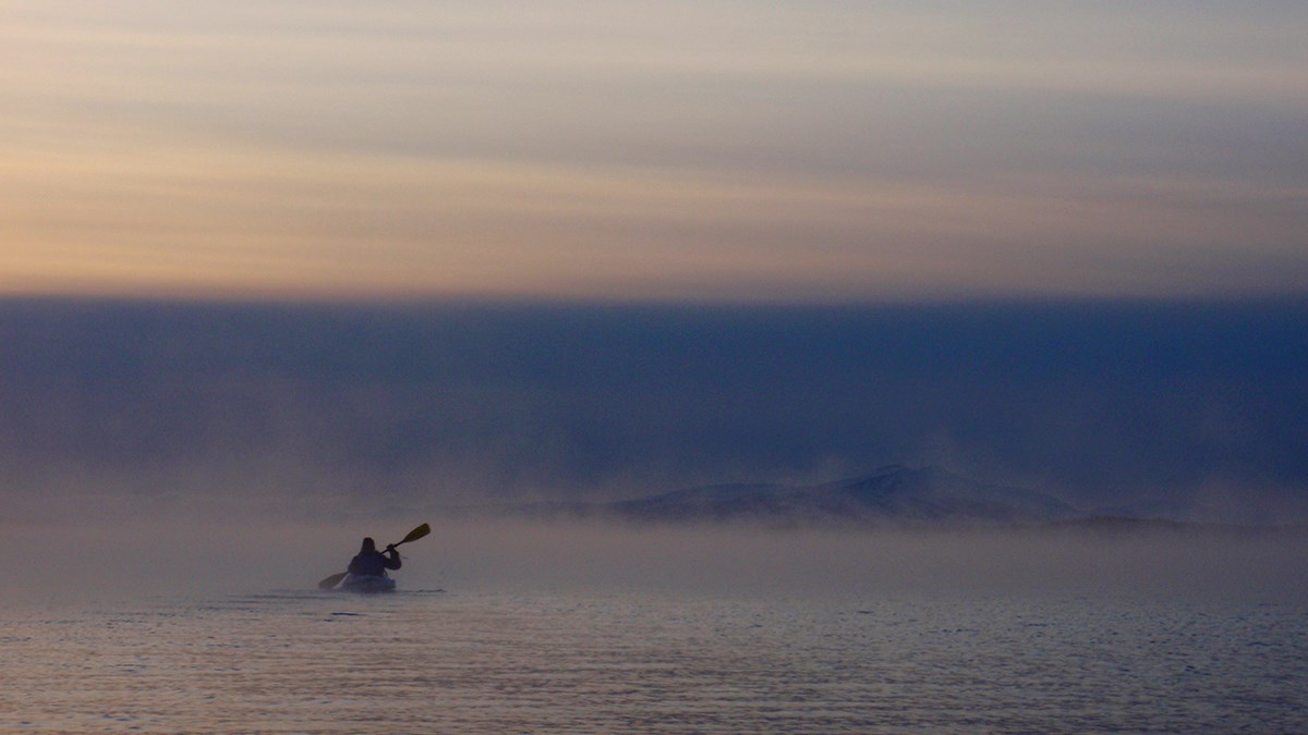 One person kayaking across a foggy lake with steam rising off the water.