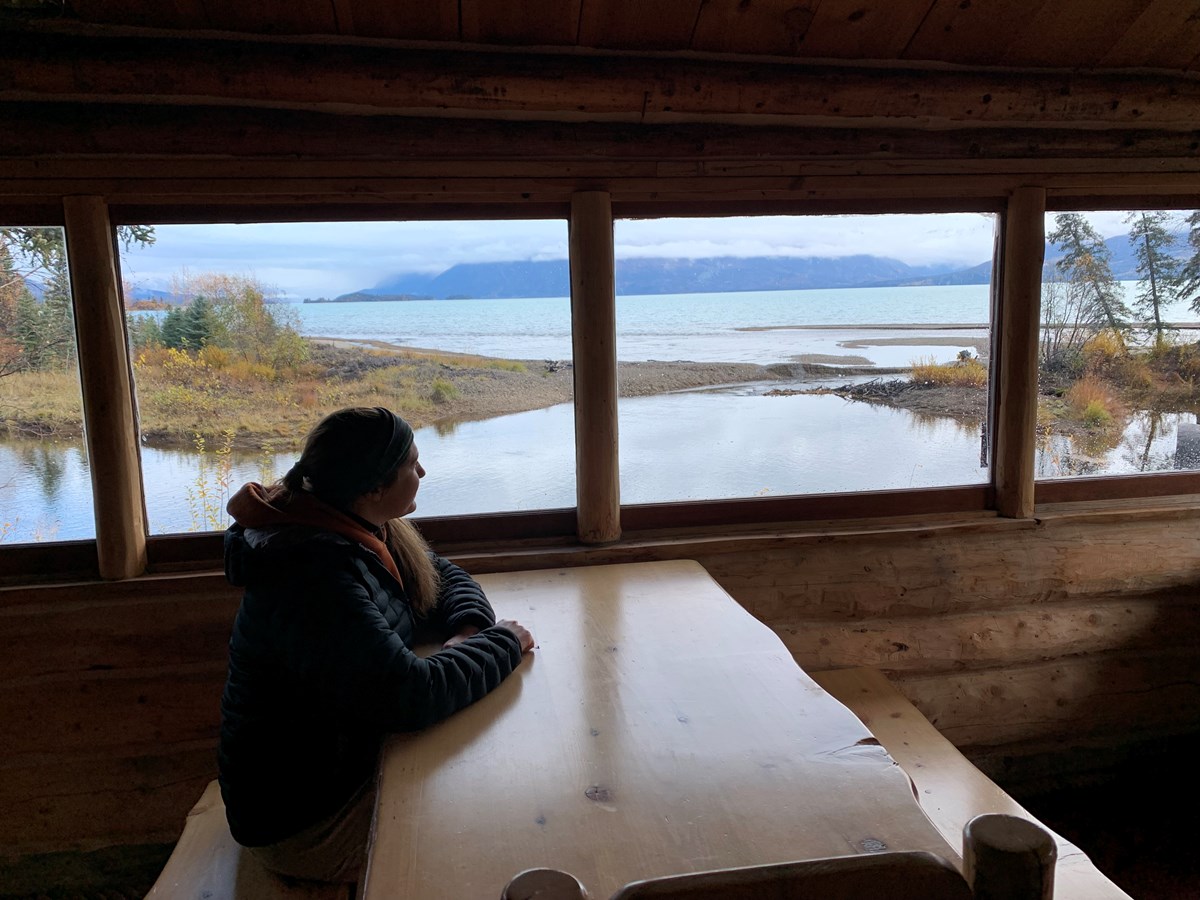 a woman sitting at a table looks out the cabin windows to the lake outside