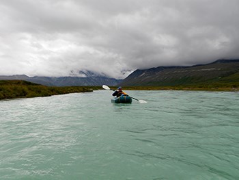 photo of a person paddling down a river in an inflatable raft with heavy clouds overhead.