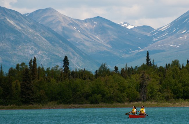 Two people canoeing on a lake with tall mountains in the background