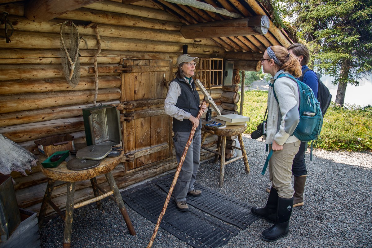 a park volunteer talks to visitors in front of the Proenneke cabin
