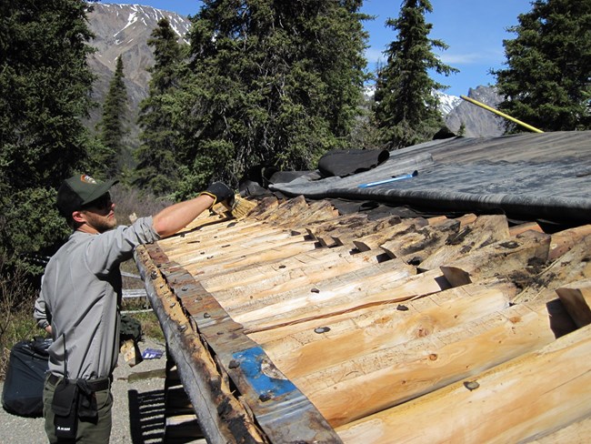 a ranger works on an exposed cabin roof
