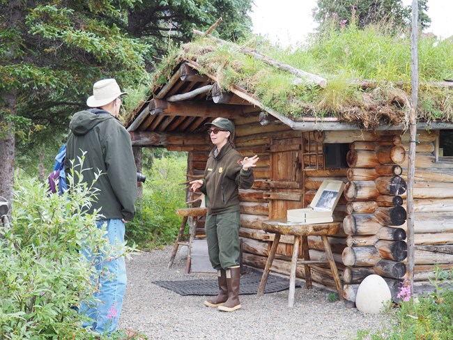 A ranger gives a tour to a group of visitors in front of the Richard L Proenneke log cabin