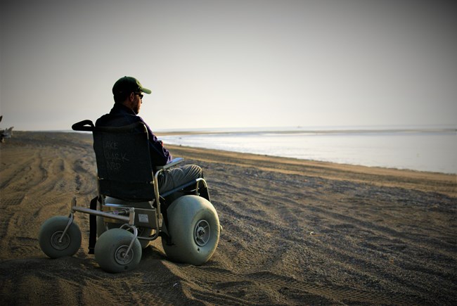 a man sits in a dune buggy wheelchair on a sandy beach