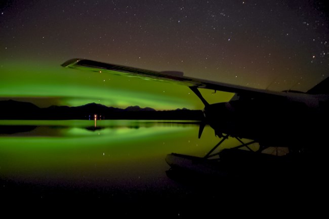 a floatplane silhouette with green northern lights behind it