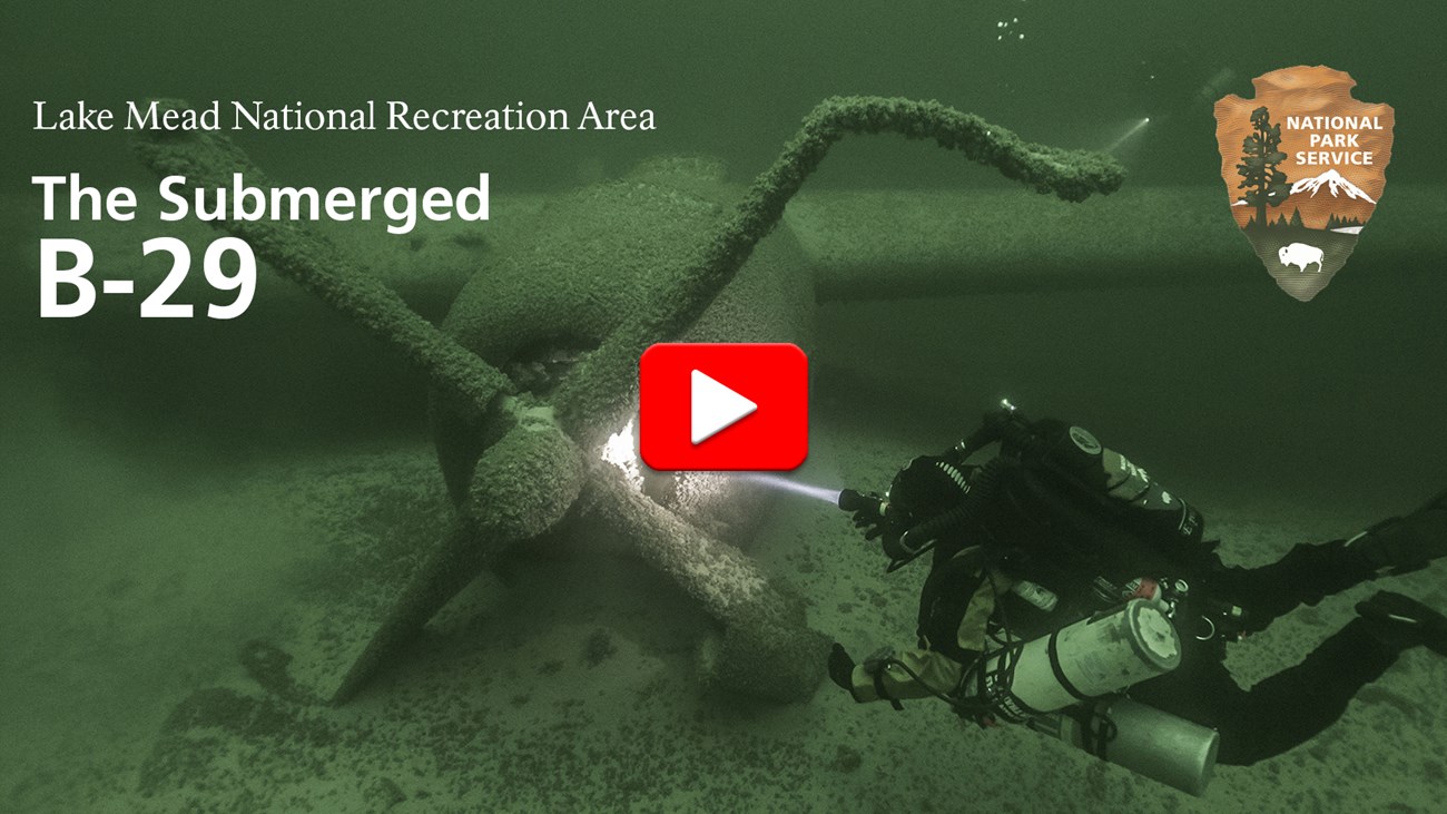 Title frame of video shows a diver swimming up to submerged B-29 plane resting on the bottom of the lake. The diver is illuminating the propellers of the plane with a headlamp. A second diver is illuminating the tail of the plane in the distance.