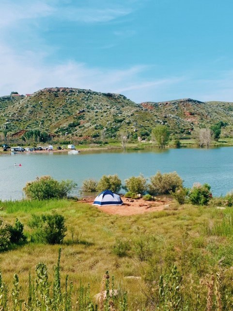 View of the lake and campgrounds.  There is a blue and white tent near the water.