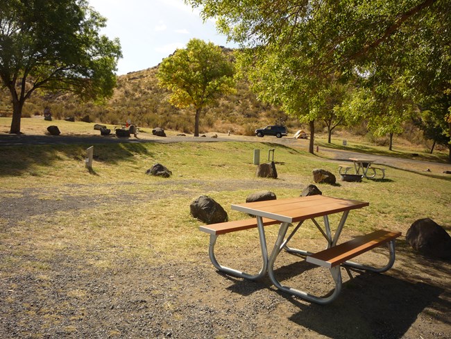 A picnic table on a rocky grassy campground, boulders are around the campsite boundary.