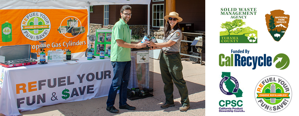 A man and a woman standing holding small propane cylinders in front of a colorful booth/display