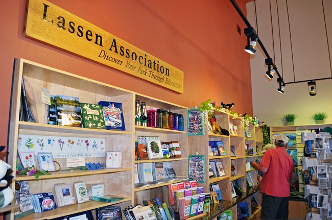 shelves with books, maps, and other retail items with a few people browsing; sign above reads "Lassen Association; Discover Your Park Through Education"