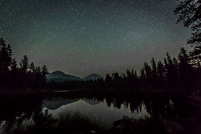 Lassen peak silhouette against a sky full of stars; scene reflected into lake in foreground