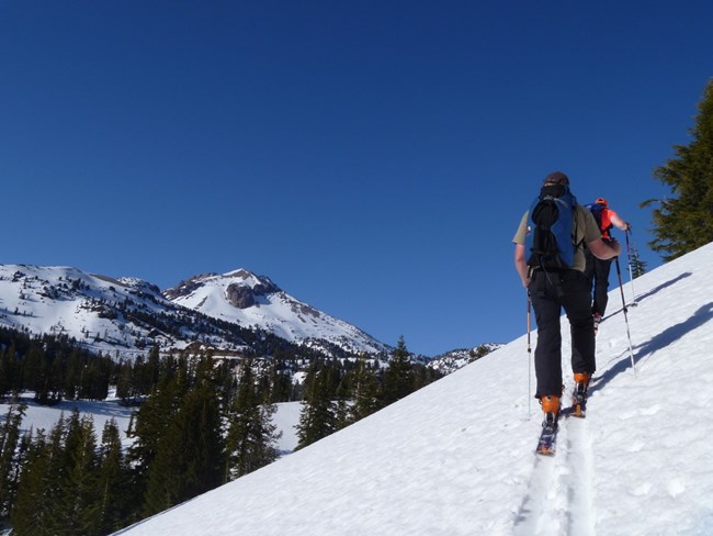 two cross-country skiers along a snowy slope, sweeping mountain view to their left