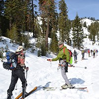 A man skis past another man holding a beacon out toward him