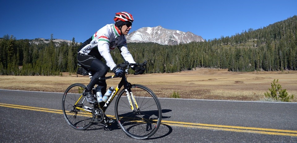 A man rides a road bike on a road in front of a meadow and gray mountain