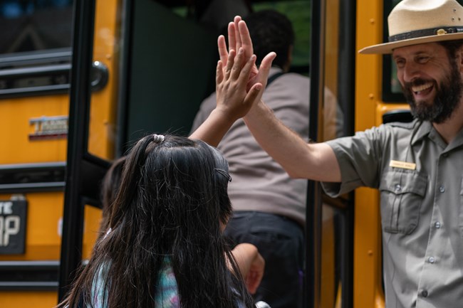 Girl high-fives with a park ranger before boarding school bus.