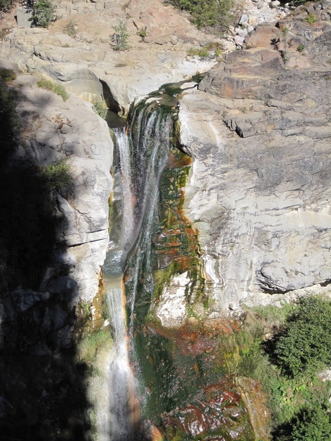 tall waterfall over pale and mossy-green rocks