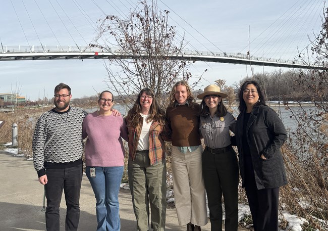 six people stand outside in front of a bridge