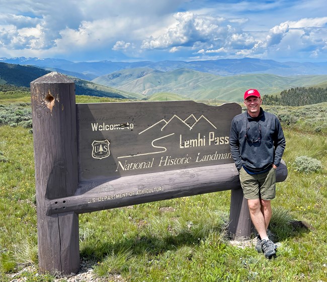 a man stands next to a sign in front of a vast grassy landscape