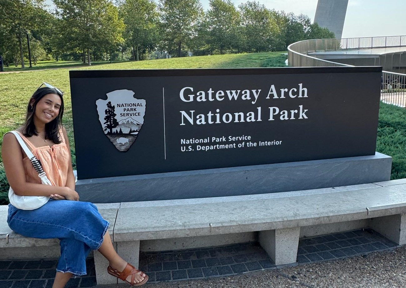 a woman sits near an outdoor sign