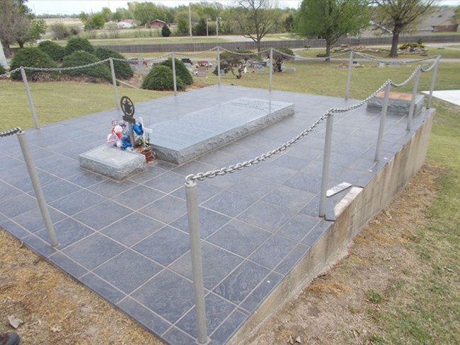 A large granite-tiled grave with poles and chain around the parameter.