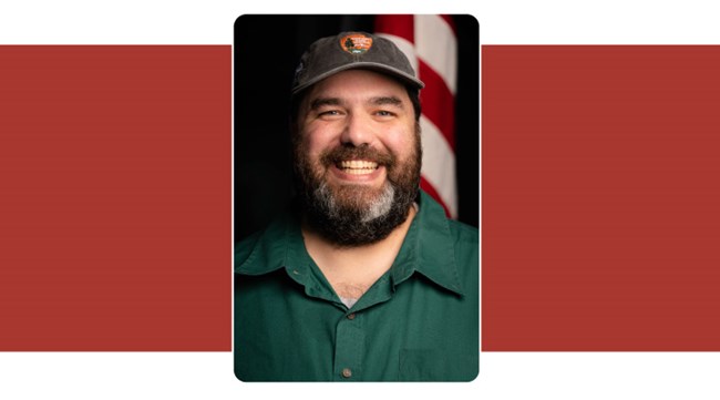 portrait of man with dark brown beard, smiling. American Flag background