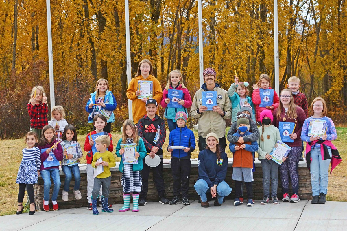 a class of kids and a few adults pose against golden aspens and hold up blue booklets